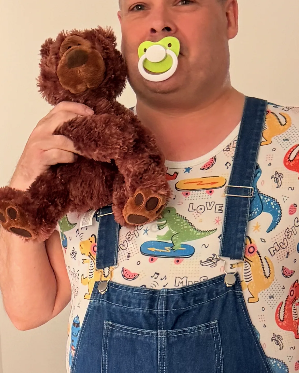 Glad voksen lille dreng i overalls med sut i munden og bamse i favnen